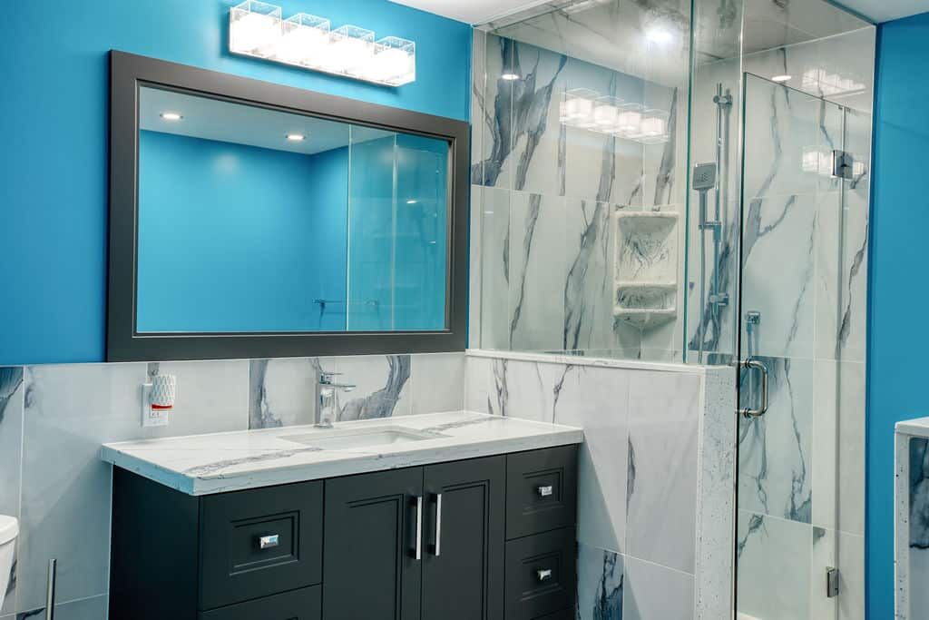 Custom bathroom design featuring a modern vanity with a marble countertop, large mirror, and glass shower enclosure against a vibrant blue wall.