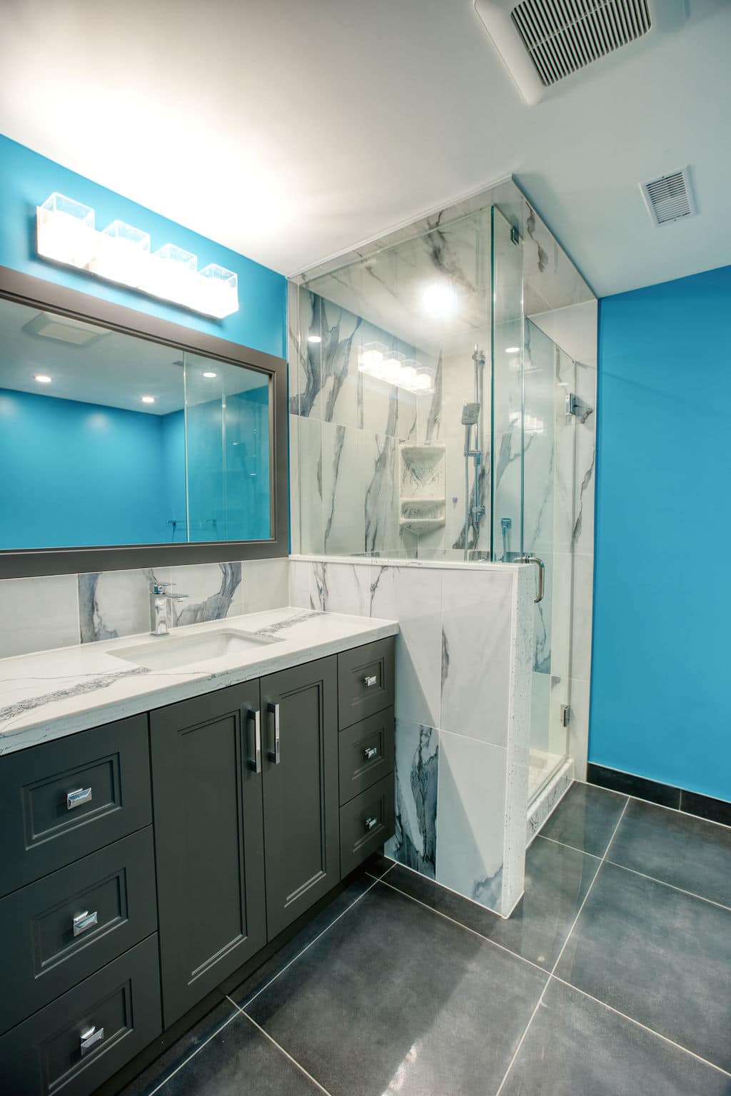 Custom bathroom design featuring a modern gray vanity with a marble countertop, glass shower enclosure, and vibrant blue walls, showcasing Superior Bath's renovation expertise.