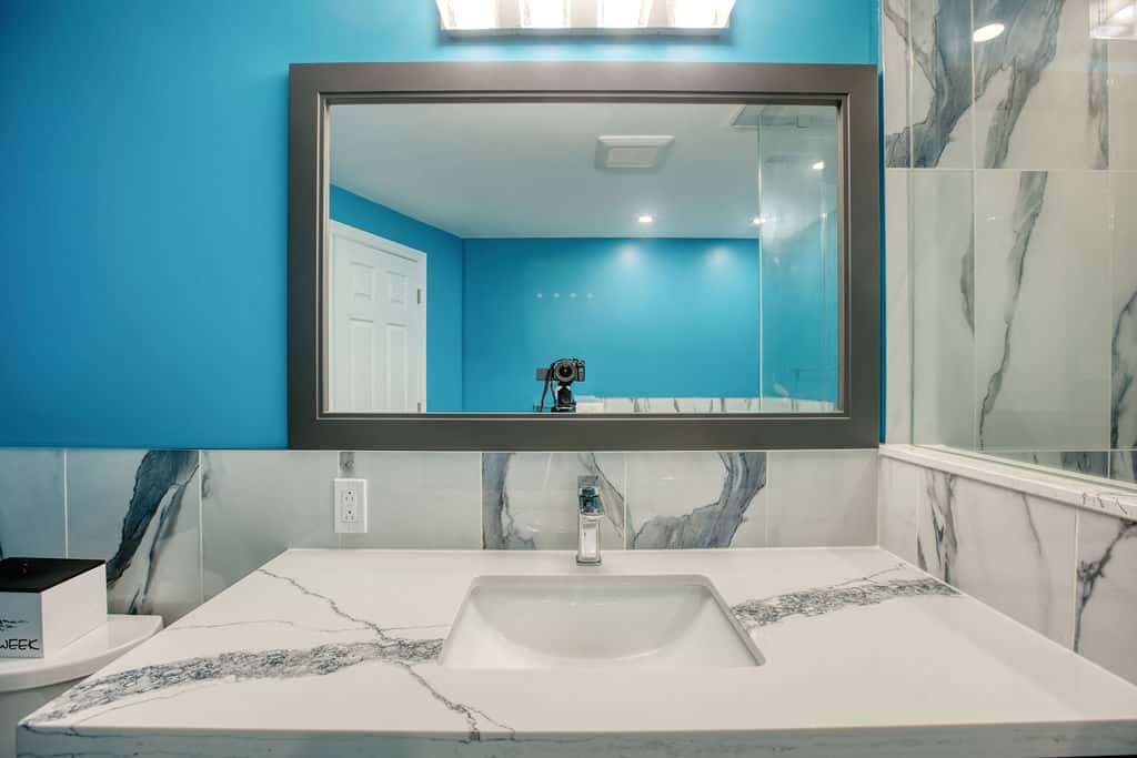 Modern bathroom with blue walls, marble countertop, sleek faucet, and large mirror showcasing contemporary design elements by Superior Bath.