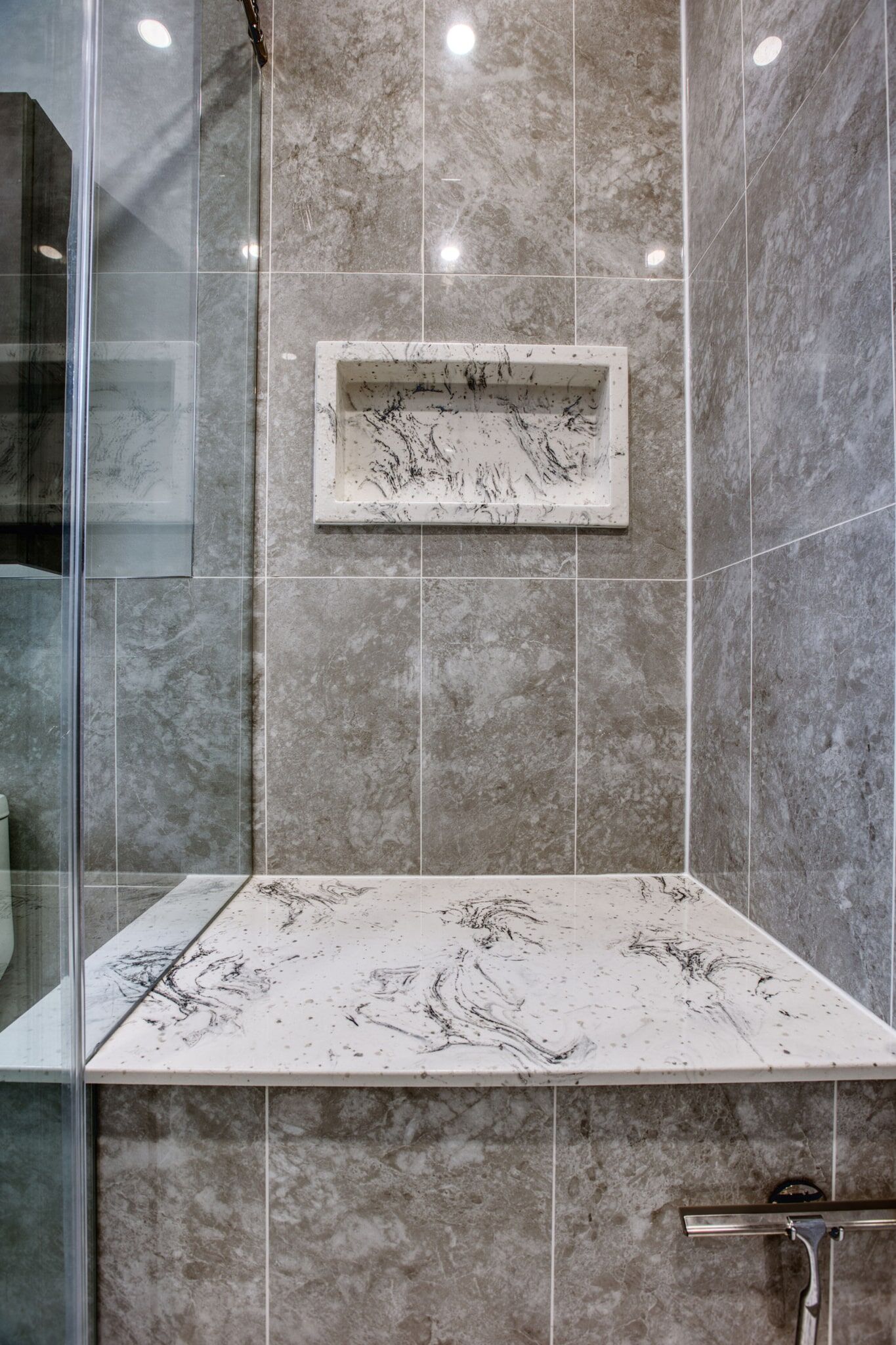 Custom bathroom renovation featuring elegant gray marble tiles and a built-in shelf in a modern shower space.